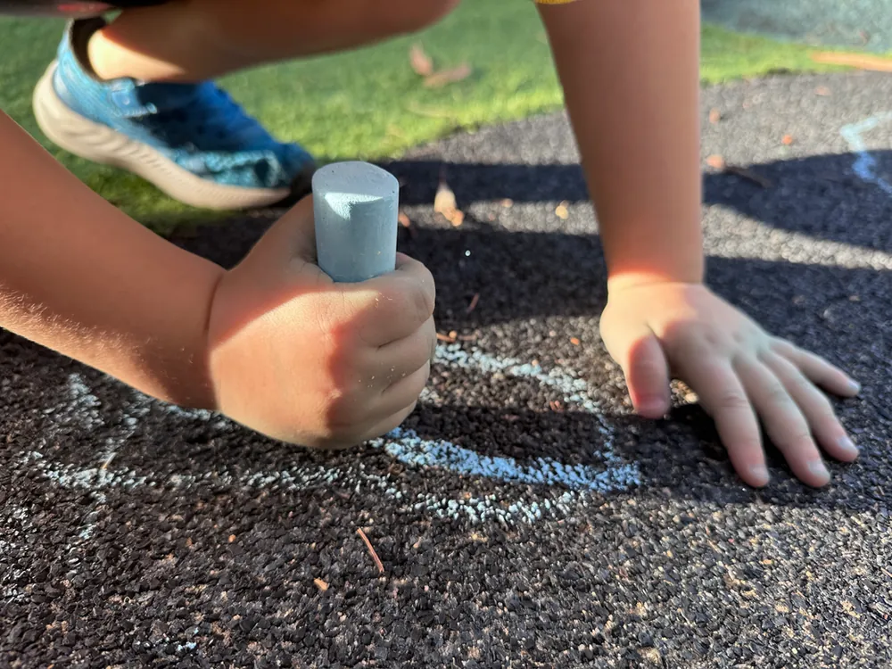 Child drawing with chalk on the ground at Little Jungle Early Learning, Dundas