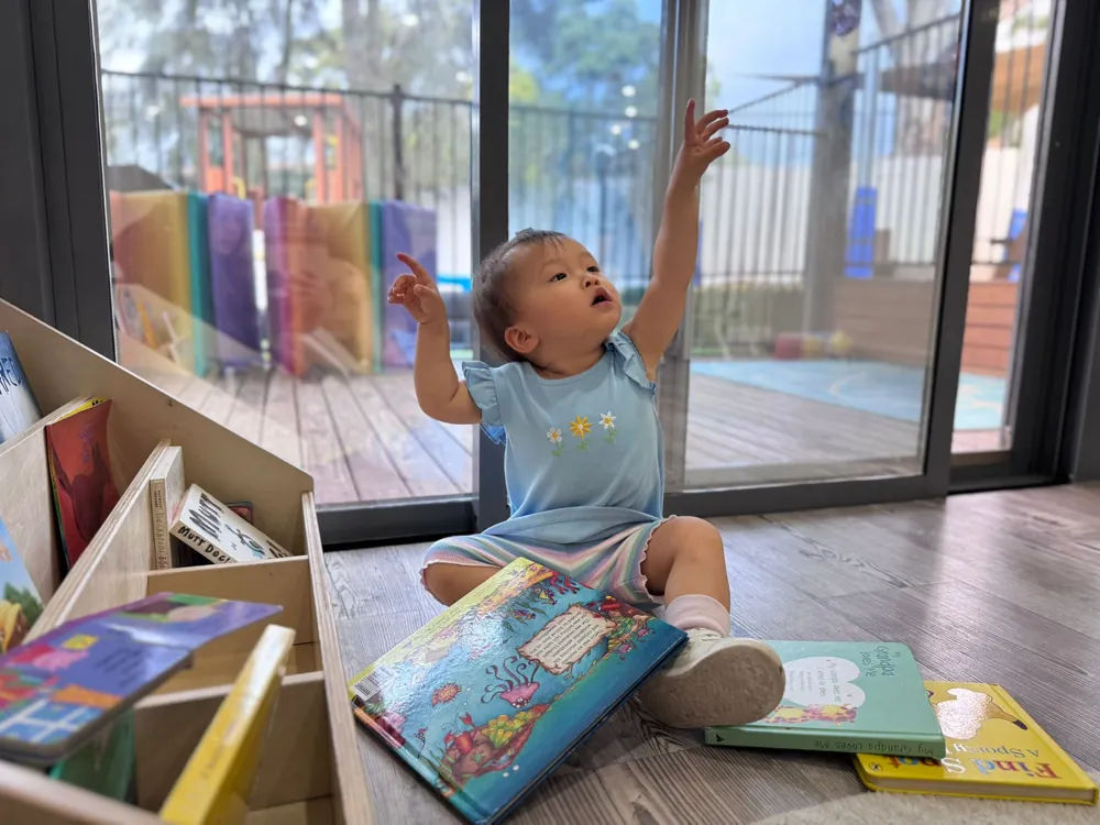 Baby looking at a picture book by the window in the Cuddle Cubs room at Little Jungle Early Learning, Dundas