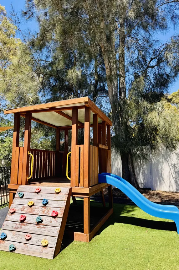 Timber cubby house with a slide and climbing wall under the gum trees