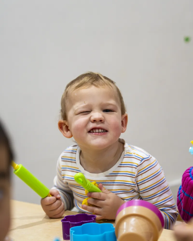Smiling toddler with a rolling pin in the Tiny Tigers room, Little Jungle Dundas